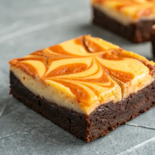 Craving Cream Cheese Brownies? Try This Halloween Swirl Twist 3 Cream cheese brownies with an orange swirl on a gray surface.