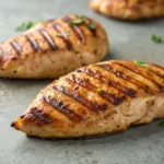 Grilled boneless chicken breasts with grill marks on gray tabletop