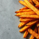 Crispy air fryer sweet potato fries piled on gray surface
