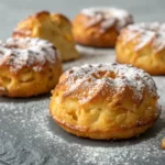 golden baked apple fritters dusted with powdered sugar on gray background